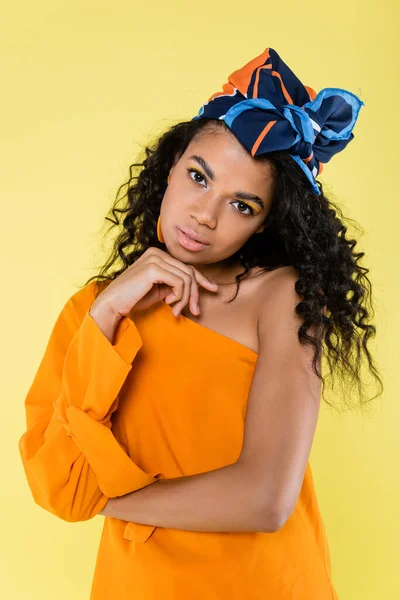 Curly african american woman in headscarf and bare shoulder posing isolated on yellow — Stock Photo