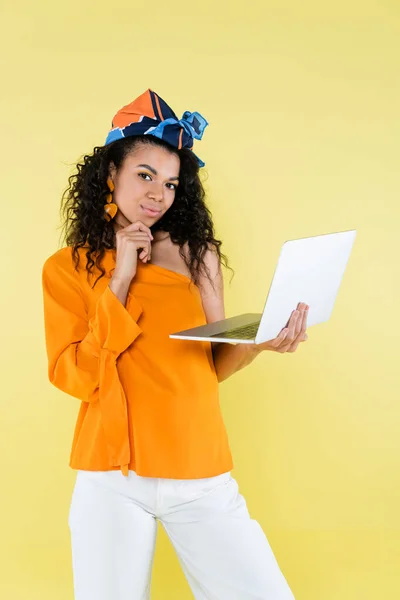 Nachdenkliche Afroamerikanerin mit Laptop isoliert auf gelb — Stockfoto