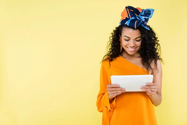 Smiling african american woman holding digital tablet isolated on yellow — Stock Photo