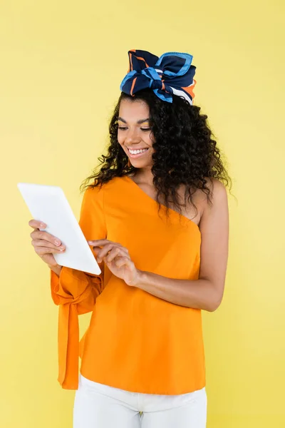 Happy african american woman holding digital tablet isolated on yellow — Stock Photo