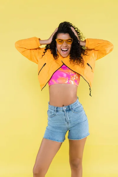 Étonnante et frisée afro-américaine jeune femme ajuster les cheveux isolés sur jaune — Photo de stock