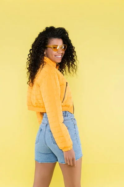 Heureux afro-américain jeune femme en lunettes de soleil isolé sur jaune — Photo de stock