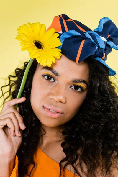 Encaracolado afro-americano mulher em kerchief segurando flor isolada em amarelo — Fotografia de Stock