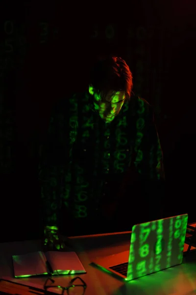 Programmer with reflection of computer code looking at laptop isolated on black — Stock Photo