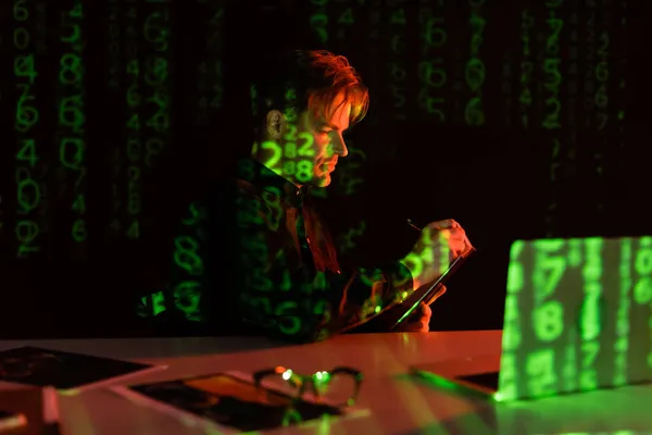Side view of programmer writing on clipboard near laptop with reflection of computer code on black background — Stock Photo