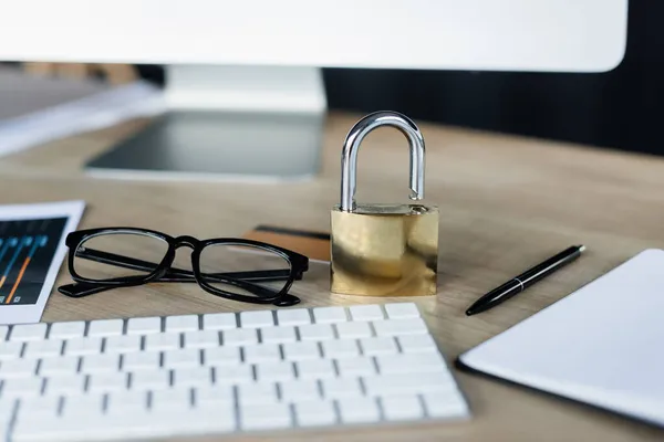 Padlock near eyeglasses and computer on table in office — Stock Photo