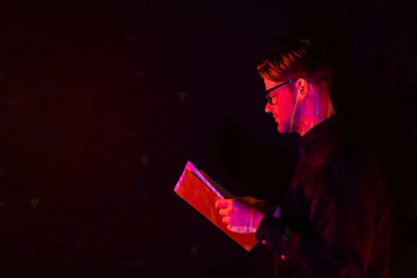 Side view of programmer holding paper folder isolated on black — Stock Photo