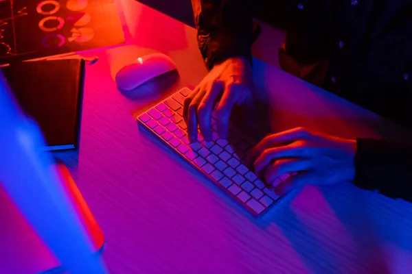 Cropped view of programmer using computer near notebook and paper on black background — Stock Photo