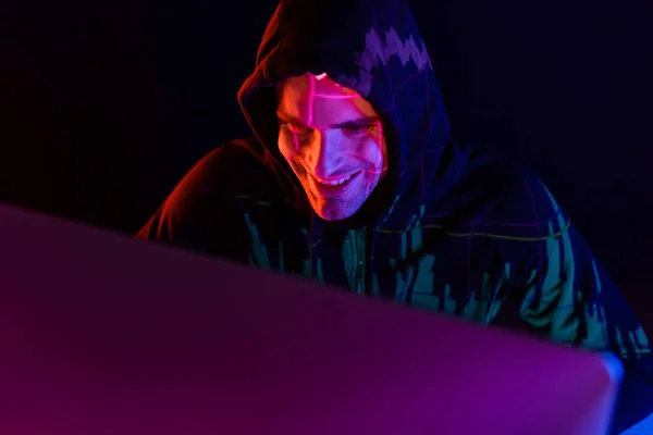 Smiling hacker with reflection of charts using computer isolated on black — Stock Photo