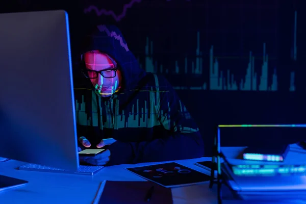 Hacker with charts reflection using smartphone near computer and documents on black background — Stock Photo