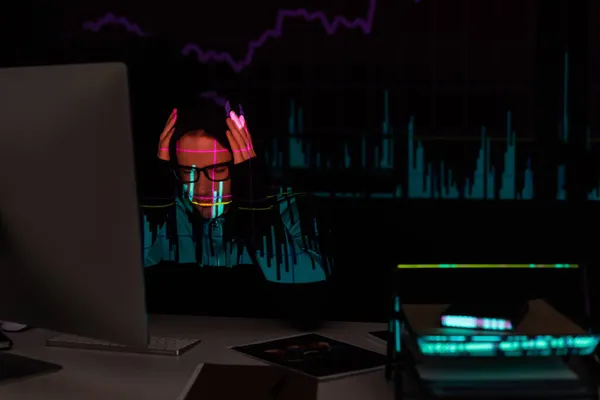 Hackeador molesto con gráficos de reflexión sentado cerca de la computadora y documentos sobre fondo negro - foto de stock