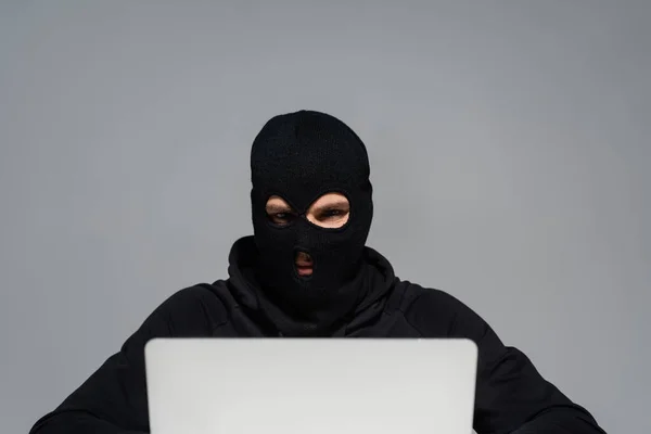 Hacker em balaclava olhando para laptop isolado em cinza — Stock Photo