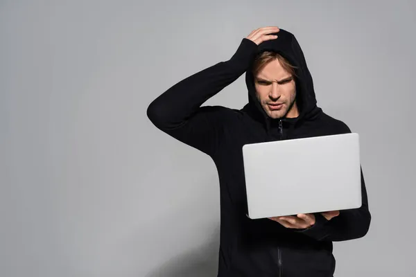 Young hacker looking at laptop on grey background — Stock Photo