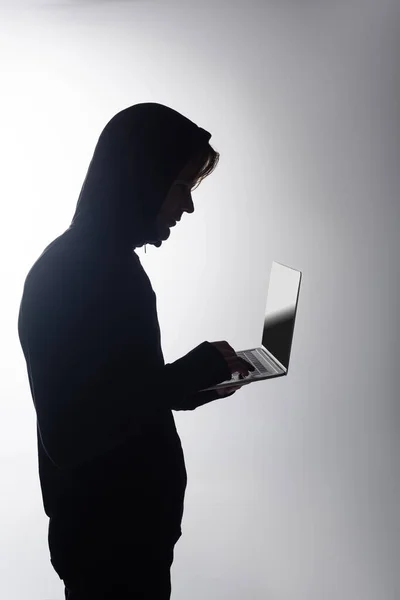 Side view of hacker in hood using laptop isolated on grey — Stock Photo