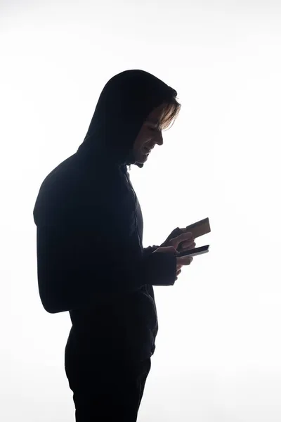 Vista lateral del hacker que sostiene el teléfono celular y la tarjeta de crédito aislados en blanco - foto de stock