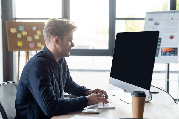 Vista laterale del programmatore utilizzando il computer vicino al caffè per andare in ufficio — Foto stock