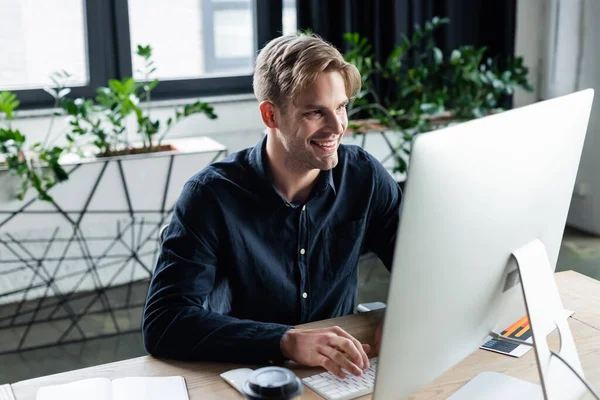 Programador positivo usando computadora cerca de notebook y café para ir en la oficina - foto de stock