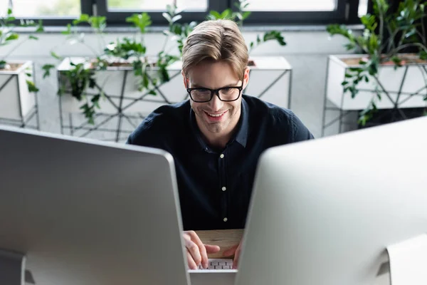 Programador feliz en anteojos usando computadoras en la oficina - foto de stock