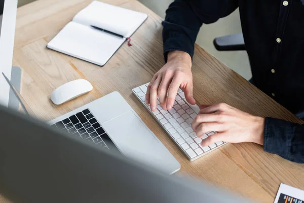 Vista ritagliata del programmatore che digita sulla tastiera del computer vicino al laptop e al notebook in ufficio — Foto stock