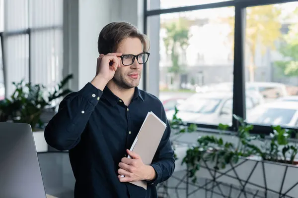 Programmer holding eyeglasses and paper folder near computer in office — Stock Photo