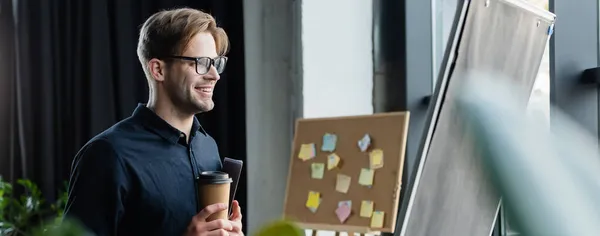 Lächelnder Programmierer mit Kaffee- und Papiermappe beim Betrachten von Flipchart, Banner — Stockfoto