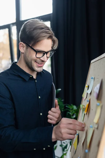Positive developer with paper folder looking at sticky notes on board — Stock Photo