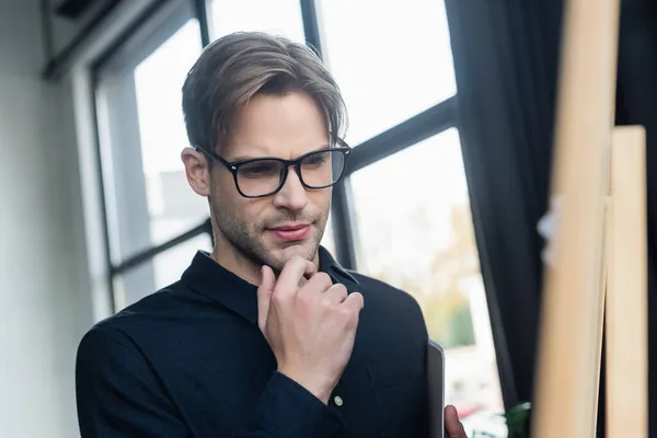 Programmeur pensif dans les lunettes regardant le tableau à feuilles mobiles dans le bureau — Photo de stock