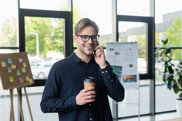 Programmeur souriant avec café parlant sur smartphone au bureau — Photo de stock