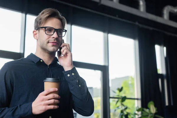 Programador hablando en el teléfono móvil y sosteniendo la taza de papel en la oficina - foto de stock