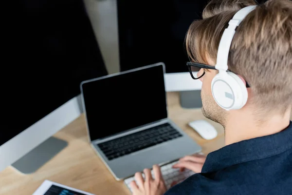 Programmeur dans les écouteurs en utilisant des ordinateurs flous près d'un ordinateur portable — Photo de stock