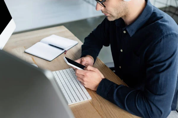 Cropped view of programmer using smartphone near computers and notebook in office — Stock Photo