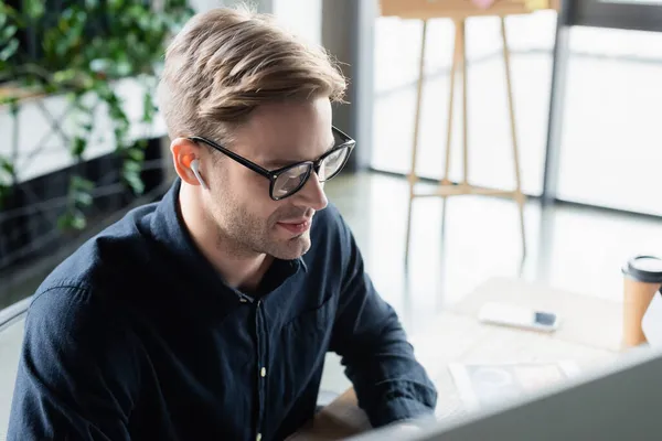 Programmer in earphone looking at blurred computer monitor in office — Stock Photo