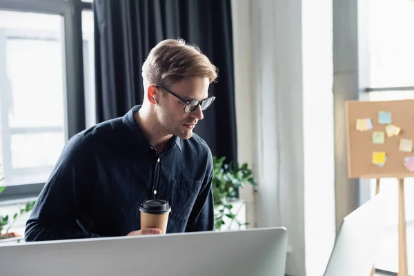 Jovem programador em fone de ouvido segurando café perto de monitores de computador — Fotografia de Stock