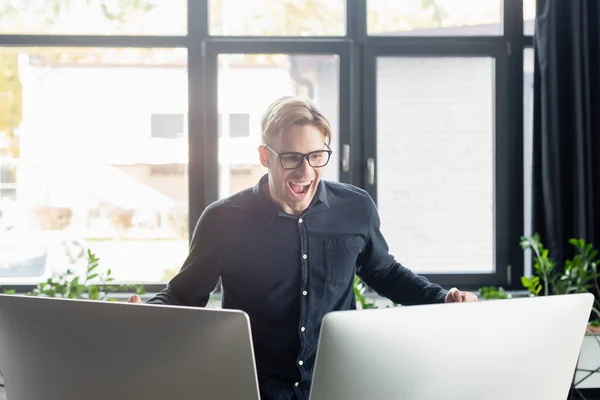 Développeur excité dans les lunettes regardant les moniteurs d'ordinateur dans le bureau — Photo de stock