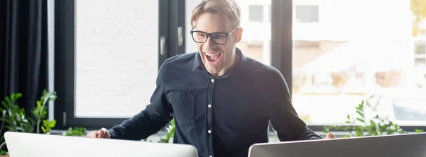 Programmeur excité dans les lunettes regardant les moniteurs d'ordinateur dans le bureau, bannière — Photo de stock