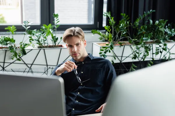 Programmer holding eyeglasses near blurred computer monitors — Stock Photo