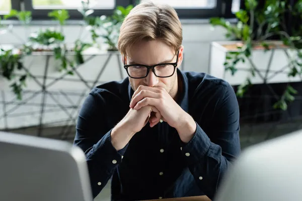 Thoughtful programmer in eyeglasses looking at computers in office — Stock Photo