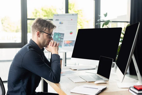 Side view of programmer looking at computers near laptop and notebooks on table — Stock Photo