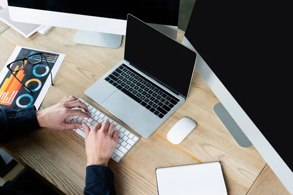 Top view of programmer typing on computer keyboard near laptop and eyeglasses on table — Stock Photo