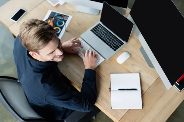 Overhead-Ansicht eines lächelnden Entwicklers mit Computern in der Nähe von Smartphone und Notebook auf dem Tisch — Stockfoto