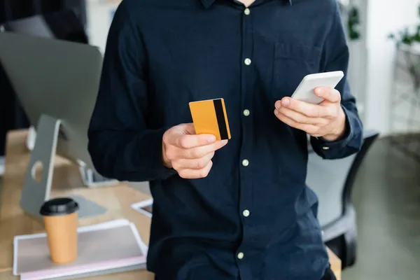 Vista cortada do programador usando smartphone e cartão de crédito no escritório — Fotografia de Stock