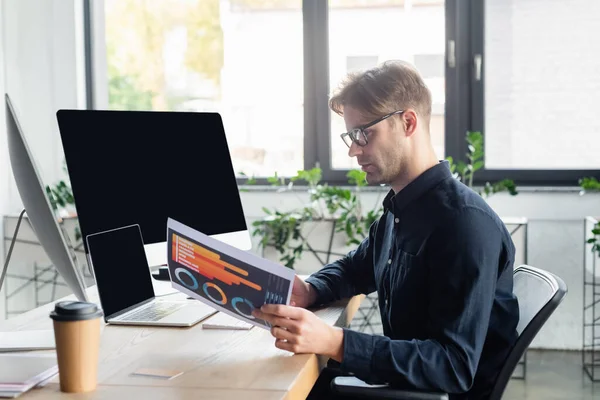 Side view of programmer working with paper near computers and coffee in office — Stock Photo