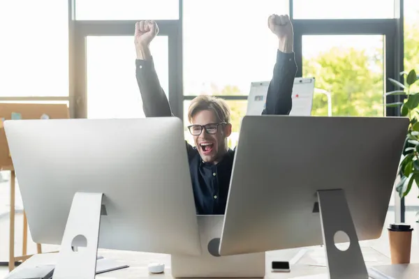 Desarrollador emocionado mostrando sí gesto cerca de computadoras en la oficina - foto de stock