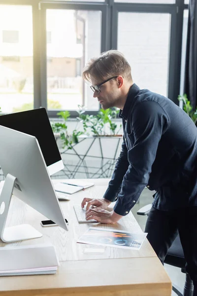 Seitenansicht des Entwicklers in Brillen mit Computern in der Nähe von Smartphone und Papier im Büro — Stockfoto