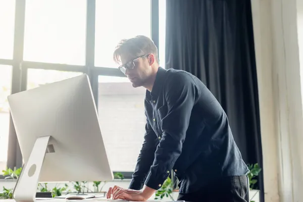 Young programmer in eyeglasses looking at computer monitor in office — Stock Photo