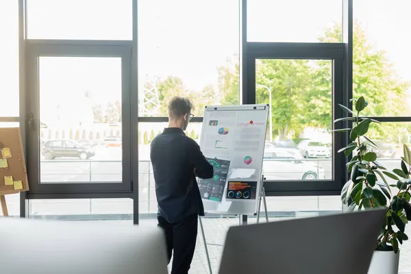 Programmeur regardant les graphiques sur flip chart près des ordinateurs flous dans le bureau — Photo de stock