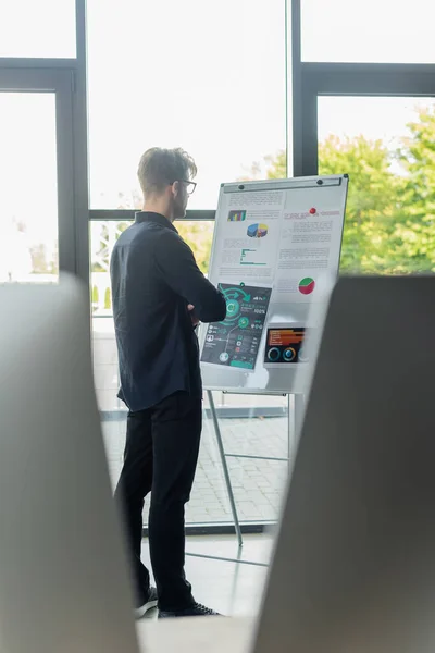 Programmer looking at graphs on flip chart near blurred computer monitors in office — Stock Photo