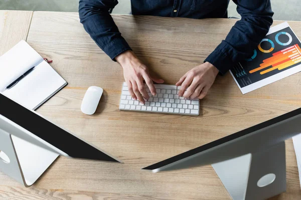 Vista superior del desarrollador utilizando el teclado cerca de computadoras y portátil en la oficina - foto de stock