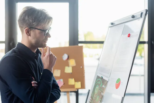 Seitenansicht eines nachdenklichen Entwicklers, der im Büro auf das Flipchart blickt — Stockfoto