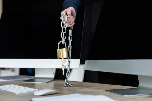 Обрезанный вид программиста, держащего замок на цепи возле компьютеров в офисе — стоковое фото